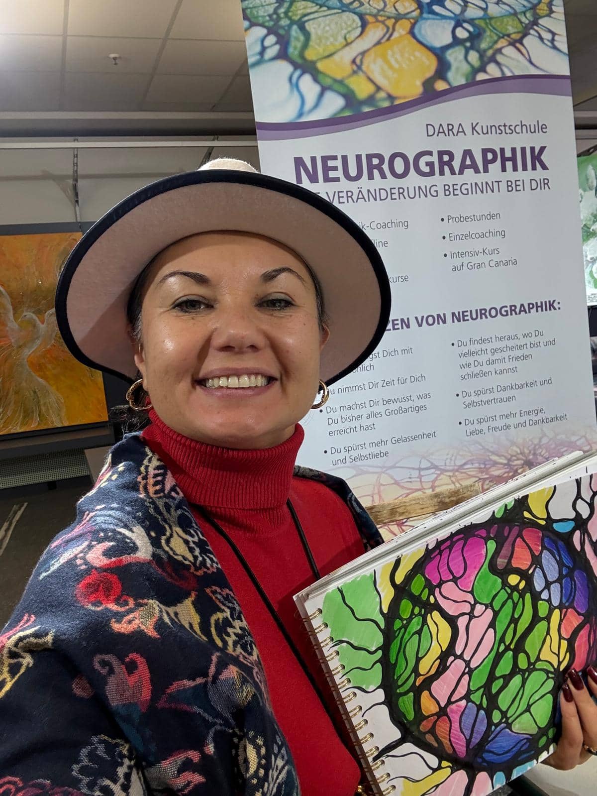 Frau zeigt ein Neurographik-Kunstwerk vor einem Banner der Dara Kunstschule